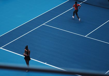 Two people playing tennis on a blue court.