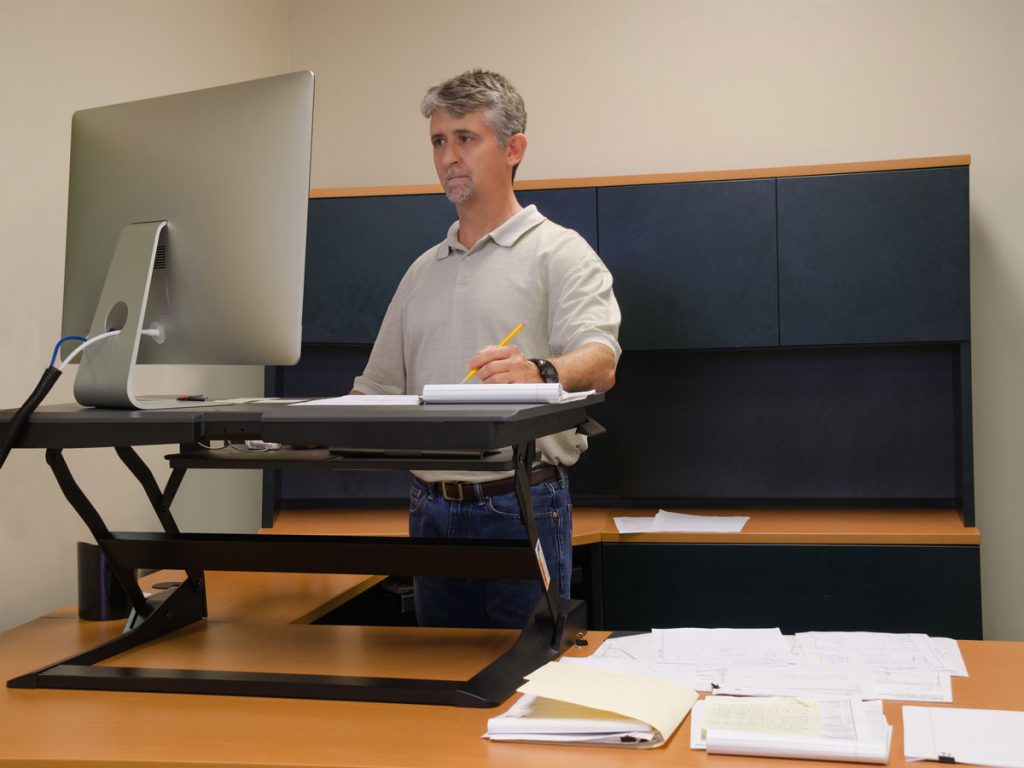 A man standing at an office desk with a laptop.