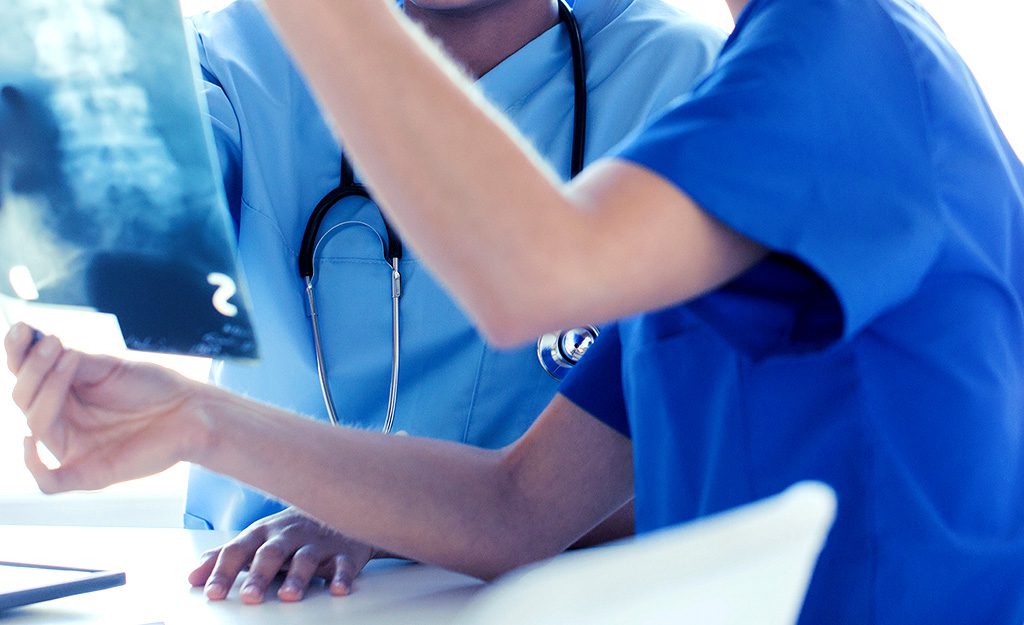 Two doctors are sitting at a table and one of them is using his hands.