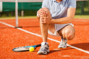 A man sitting on the ground with his tennis racket