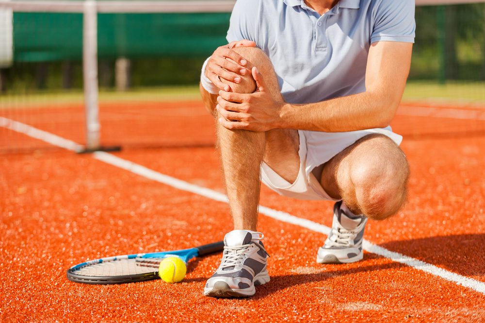 tennis player touching his knee while sitting on the tennis court