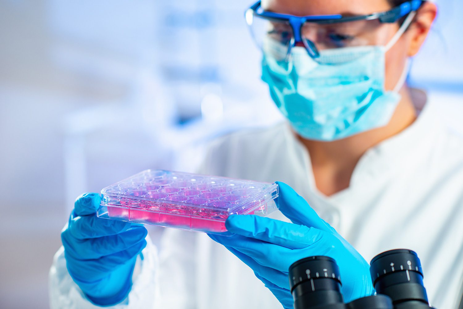 A man in lab coat holding up a pink substance.