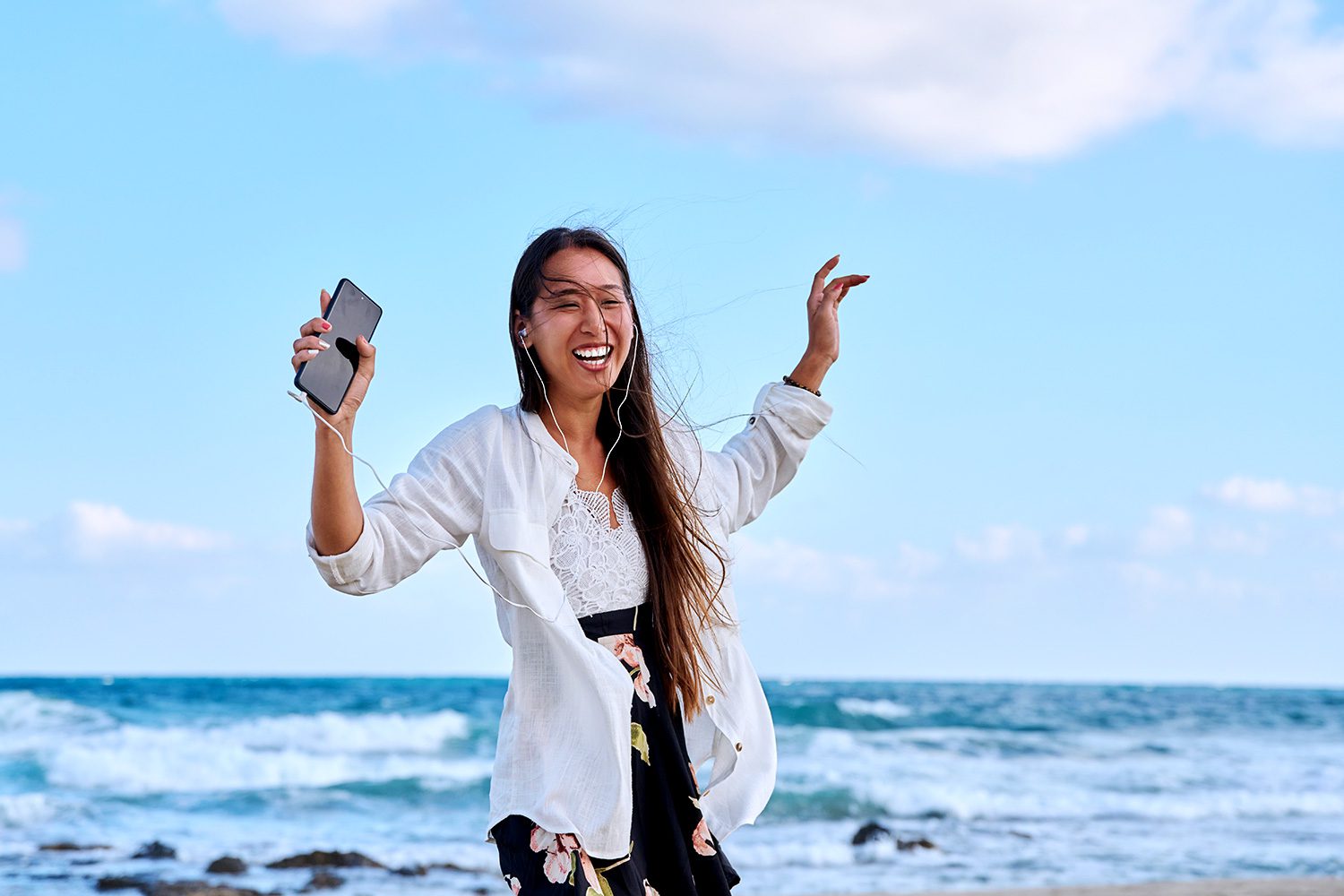 A woman holding up her cell phone on the beach.