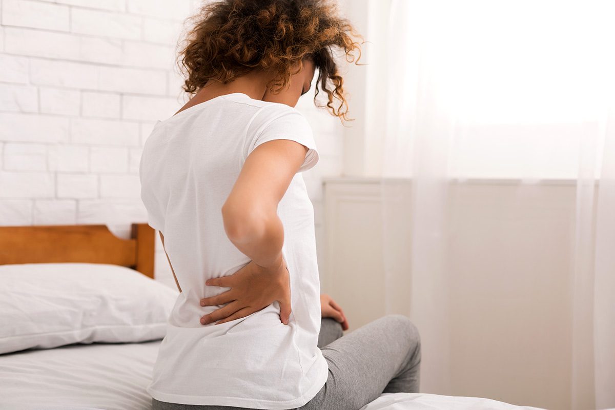 A woman sitting on top of her bed with her hands behind her back.