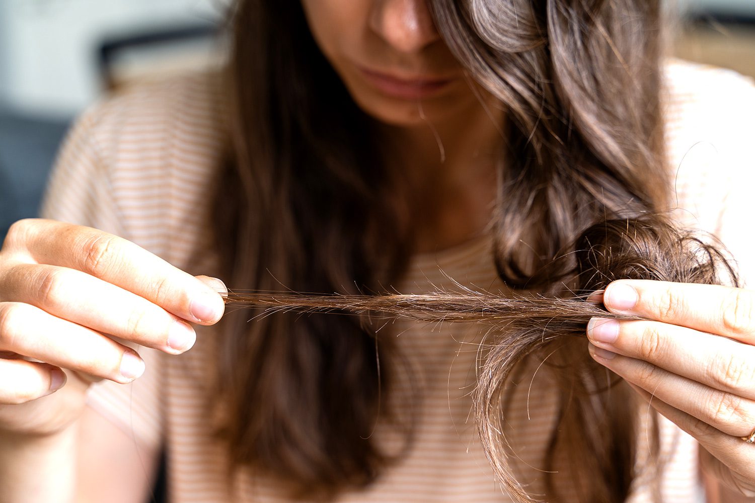 A woman is holding her hair in one hand and pulling it out of the other.