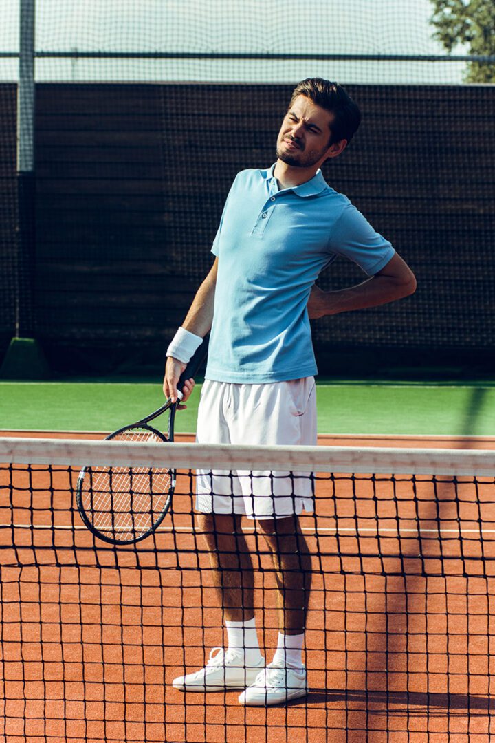 Male leaning back, tennis racket in hand, appears to be in pain. Photo is for a blog post about treatment for sports related injuries