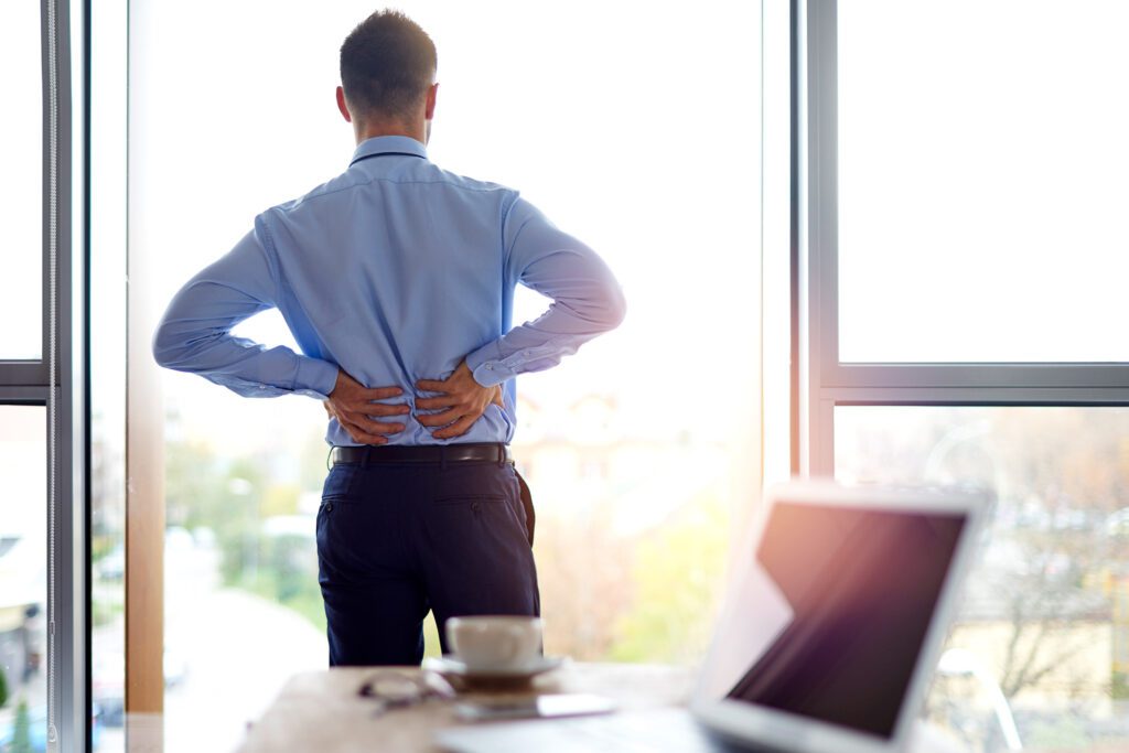 A photo of a male standing up and holding his back for a blog post by the spine and sports doctor on herniated disks and spinal fractures