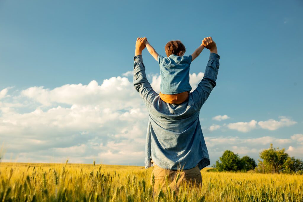 A man and his daughter are standing in a vast wheat field, enjoying the tranquility of nature and oblivious to any muscle pain they might have.